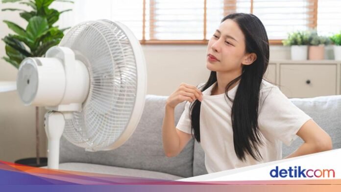 Ilustrasi seseorang menggunakan kipas untuk menghadapi cuaca panas