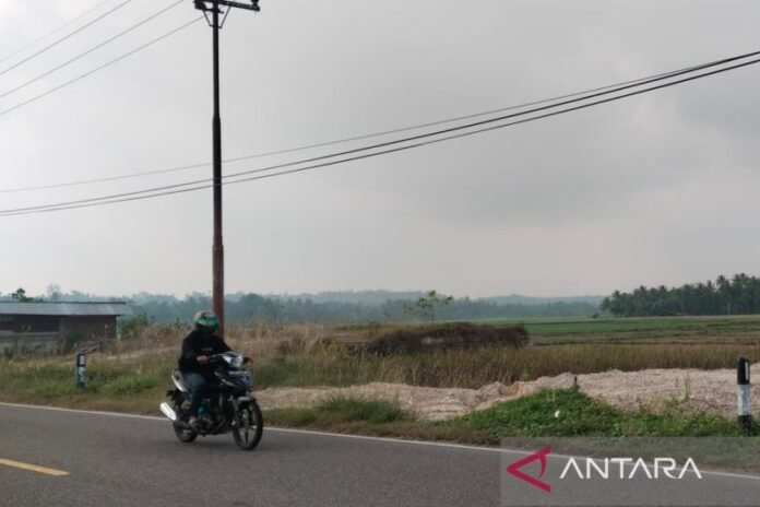 Pengendara melintas dengan latar kabut asap di Padang Pariaman, Sumatra Barat